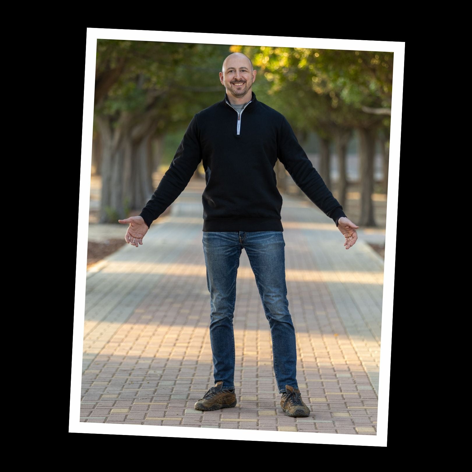 A tall slim guy wearing an extra long sweatshirt with arms spread out to show the sleeves are long enough for his lanky arms.