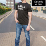 A head to toe shot of a tall skinny guy wearing a tall graphic bodybuilding t-shirt.