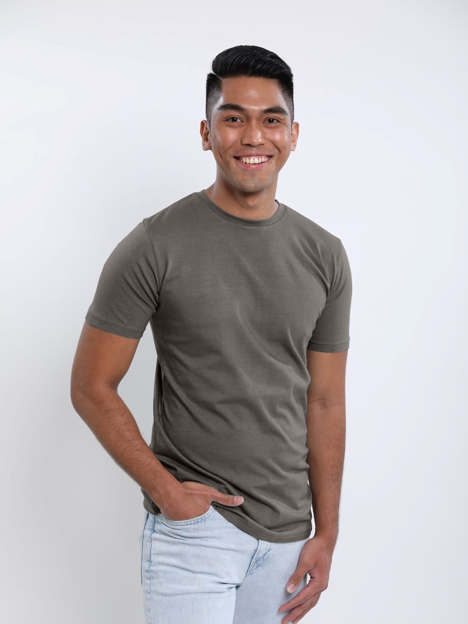 A tall and slim man in the studio standing in front of a light background. The smiling model is wearing an extra long slim dark grey t-shirt in a size medium. The tall dark grey t-shirt features a 3" longer body, 100% organic cotton, and is soft & preshrunk. The dark grey t-shirt is ideal for tall slim men 6'2"+.