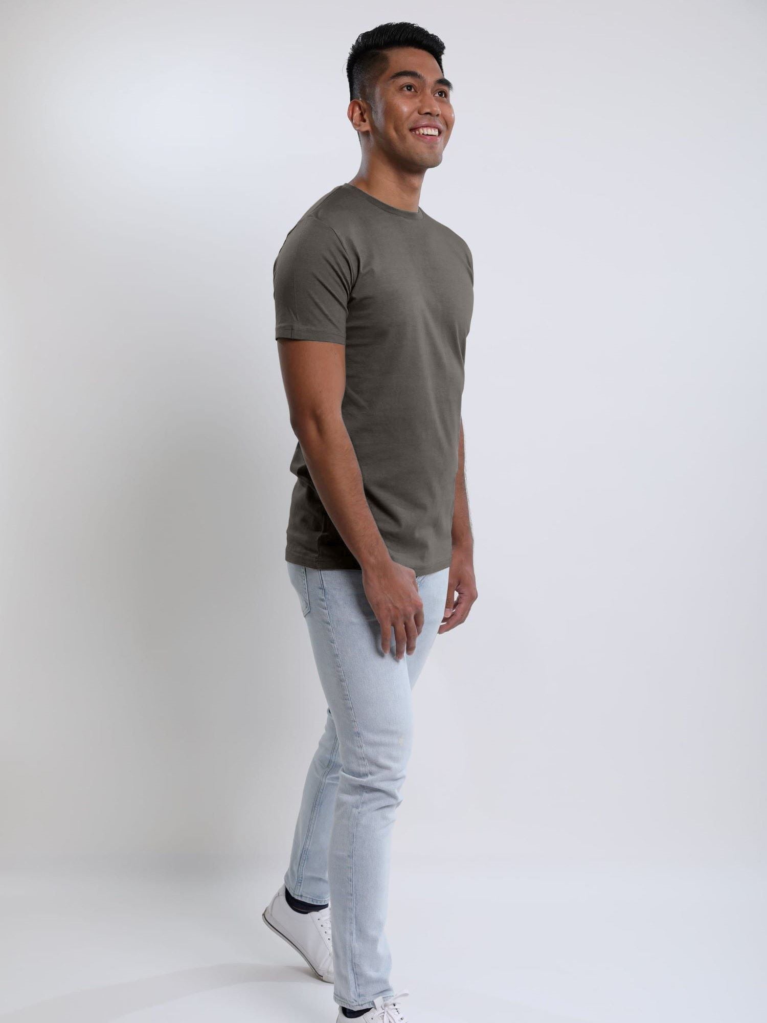 A head to toe shot of a tall slim guy in a studio and wearing a dark grey medium tall slim t-shirt.