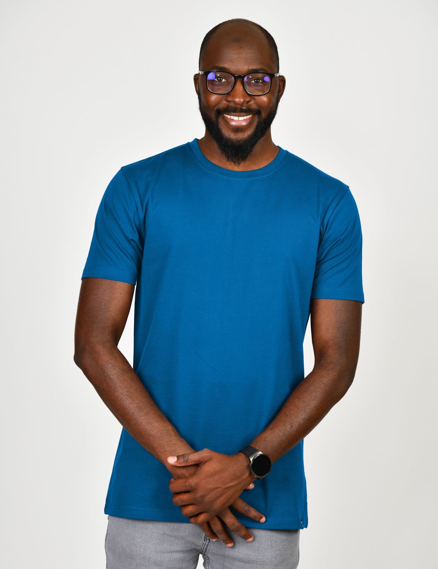 A tall and slim man in the studio standing in front of a light background. The smiling model is wearing an extra long slim azure t-shirt in a size large. The tall large t-shirt features a 3" longer body, 100% organic cotton, and is soft & preshrunk. The large t-shirt is ideal for tall slim men 6'2"+.
