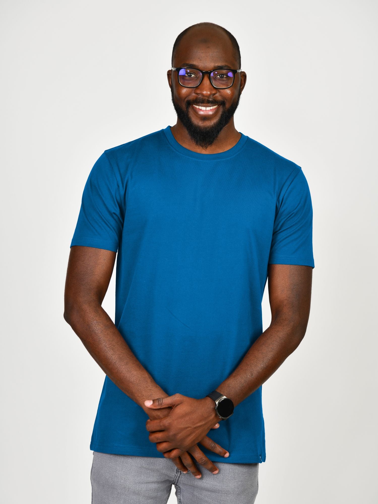 A tall and slim man in the studio standing in front of a light background. The smiling model is wearing an extra long slim azure t-shirt in a size large. The tall large t-shirt features a 3" longer body, 100% organic cotton, and is soft & preshrunk. The large t-shirt is ideal for tall slim men 6'2"+.