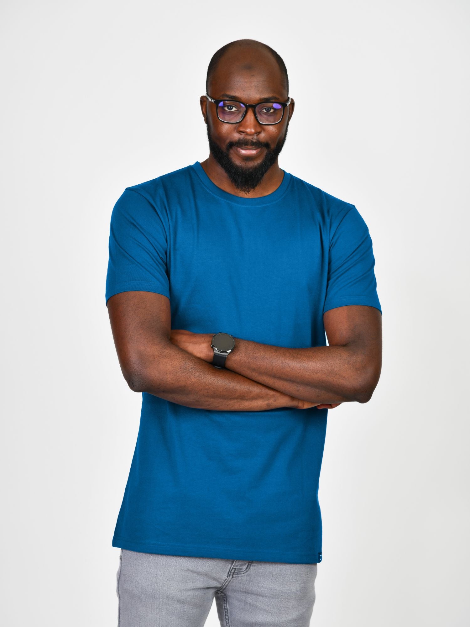 An upper body shot of a tall slim guy wearing an extra long large tall azure t-shirt, hands folded and looking serious.