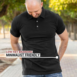 An upper body shot of a tall athletic guy in a park and wearing an XL tall slim black polo shirt and showing the minimal Just Tall flag logo near the bottom of the side seam.