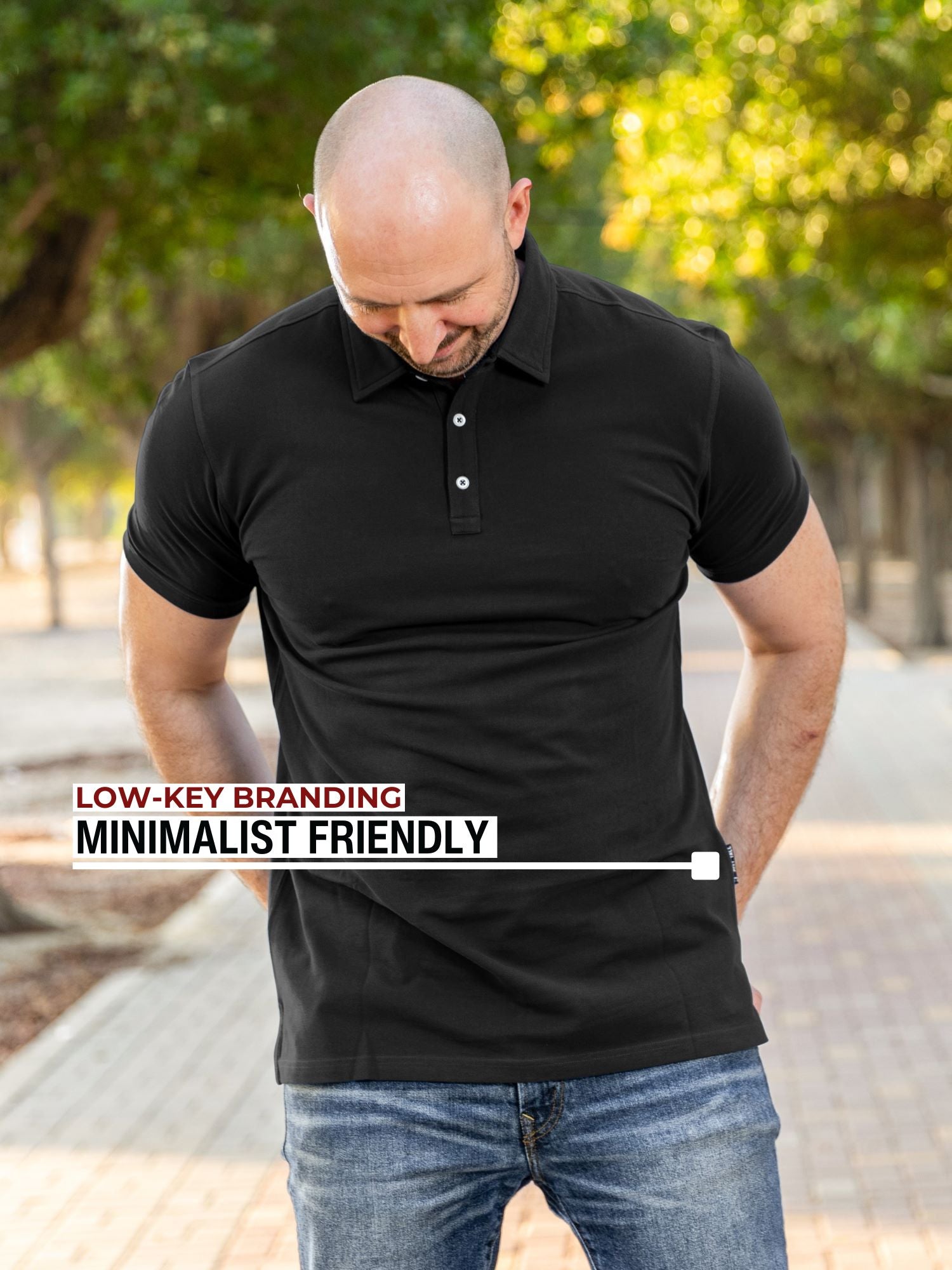 An upper body shot of a tall athletic guy in a park and wearing an XL tall slim black polo shirt and showing the minimal Just Tall flag logo near the bottom of the side seam.