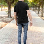 A shot from behind of a tall athletic guy in a park and wearing a black XL tall polo shirt.