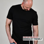 A tall athletic guy standing in a studio and wearing a black XL tall t-shirt, looking down at the Just Tall monogram logo.