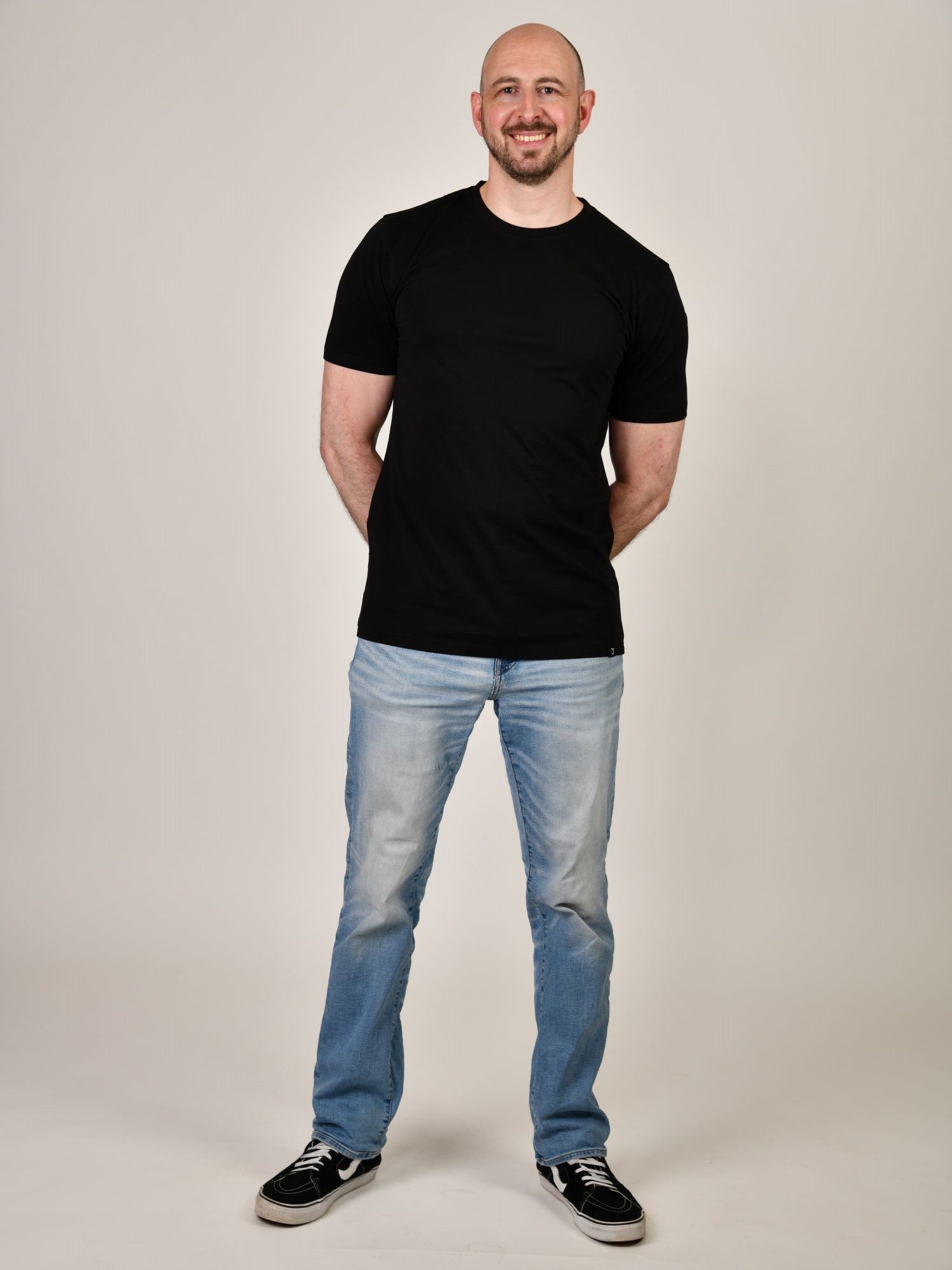 A head to toe shot of a tall and slim guy in the studio wearing a black XL tall slim t-shirt.