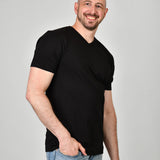 A tall and slim man in the studio standing in front of a light background with one hand in his pocket. The smiling model is wearing an extra long slim black v-neck t-shirt in a size XL. The tall black v-neck t-shirt features a 3" longer body, 100% organic cotton, and is soft & preshrunk. The black v-neck t-shirt is ideal for tall slim men 6'2"+.