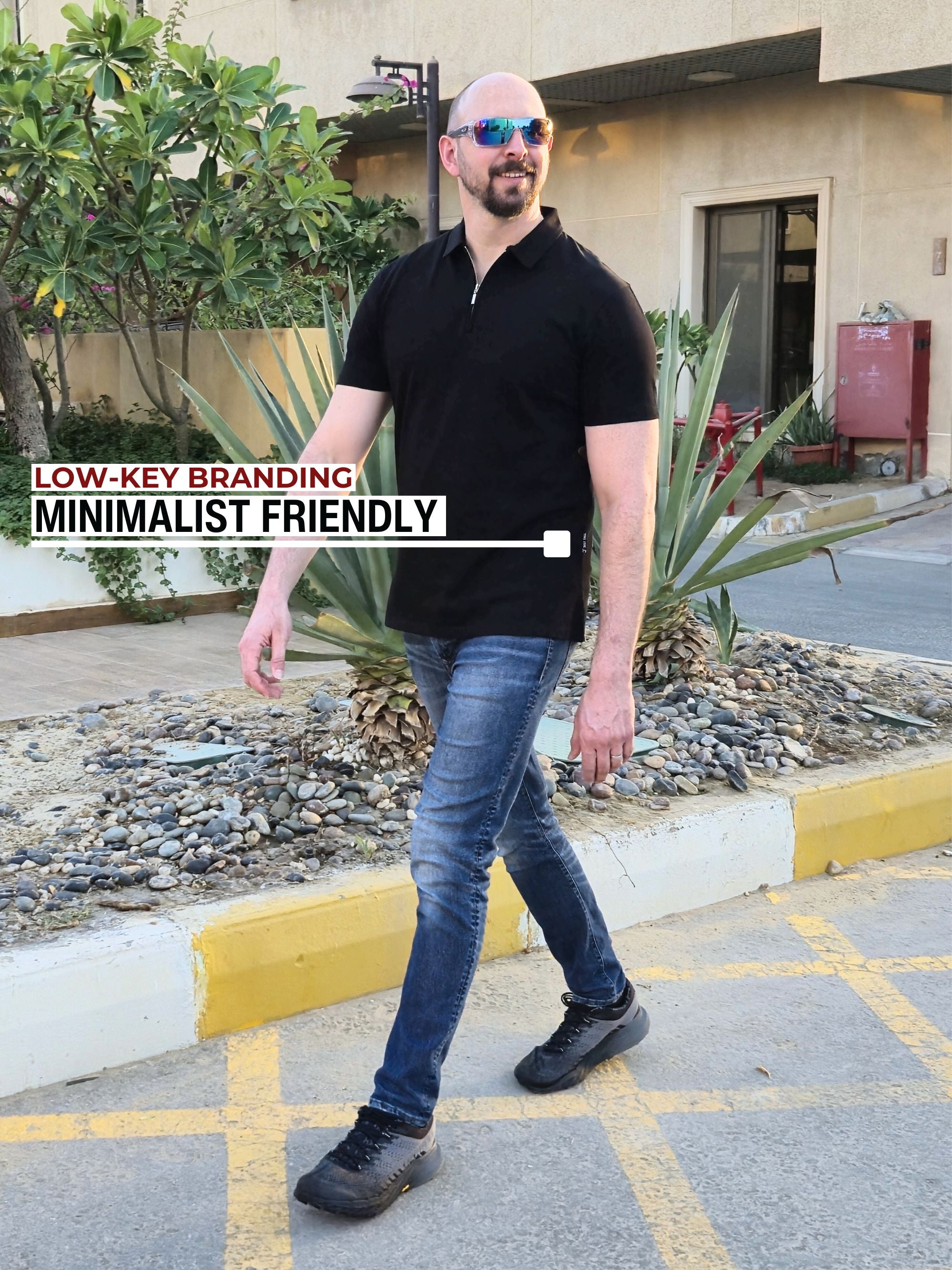 A tall slim man wearing an XL tall black zip polo shirt and walking in a residential compound.