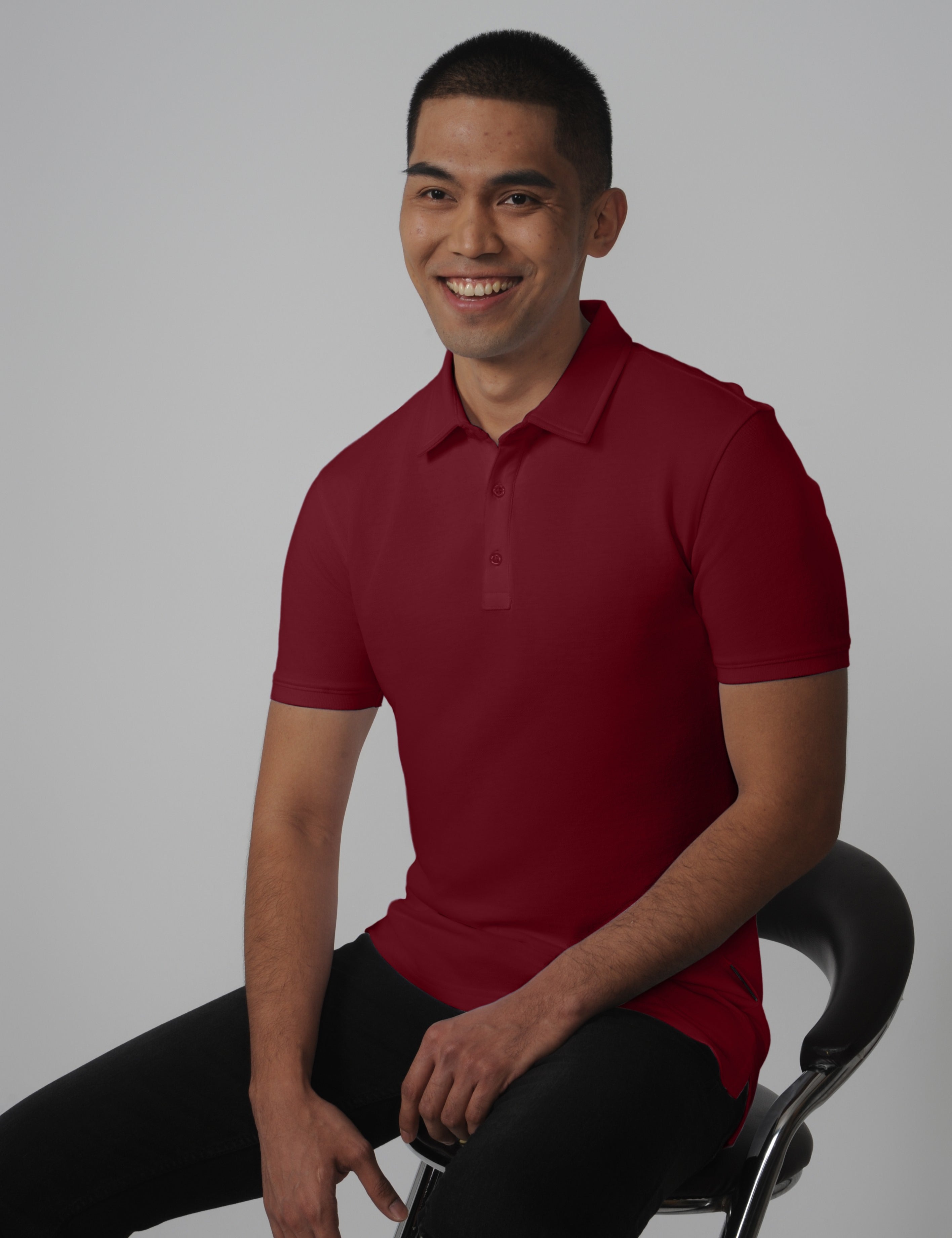 A tall slim man sitting in a studio and wearing a maroon medium tall polo shirt.