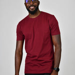 A tall and slim man in the studio standing in front of a light background. The smiling model is wearing an extra long slim cabernet t-shirt in a size large. The tall cabernet t-shirt features a 3" longer body, 100% organic cotton, and is soft & preshrunk. The cabernet  t-shirt is ideal for tall slim men 6'2"+.