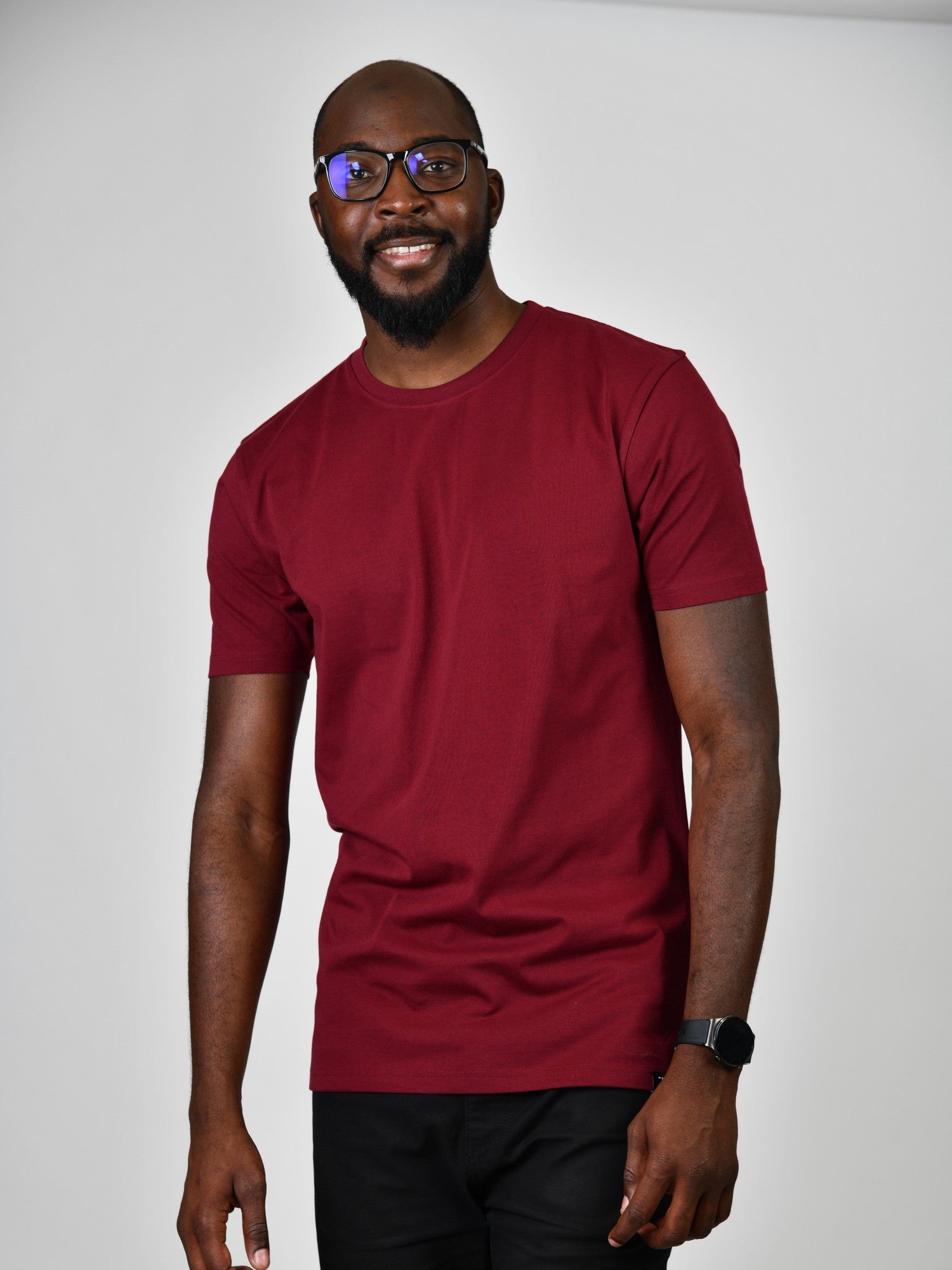 A tall and slim man in the studio standing in front of a light background. The smiling model is wearing an extra long slim cabernet t-shirt in a size large. The tall cabernet t-shirt features a 3" longer body, 100% organic cotton, and is soft & preshrunk. The cabernet t-shirt is ideal for tall slim men 6'2"+.
