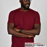 A tall slim guy standing in a studio and wearing a cabernet large tall t-shirt, smiling and hands crossed.