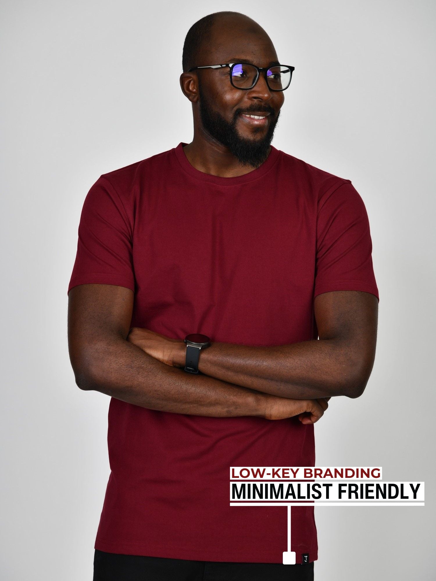 A tall slim guy standing in a studio and wearing a cabernet large tall t-shirt, smiling and hands crossed.