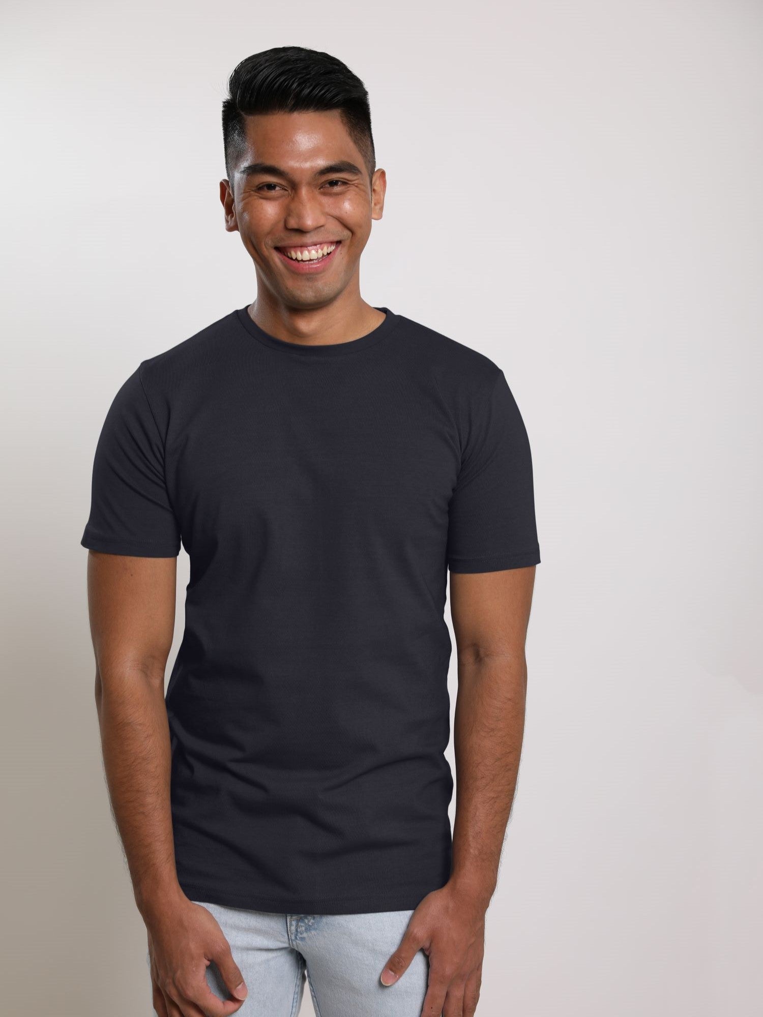 A tall and slim man in the studio standing in front of a light background. The smiling model is wearing an extra long slim charcoal t-shirt in a size medium. The tall charcoal t-shirt features a 3" longer body, 100% organic cotton, and is soft & preshrunk. The charcoal t-shirt is ideal for tall slim men 6'2"+.
