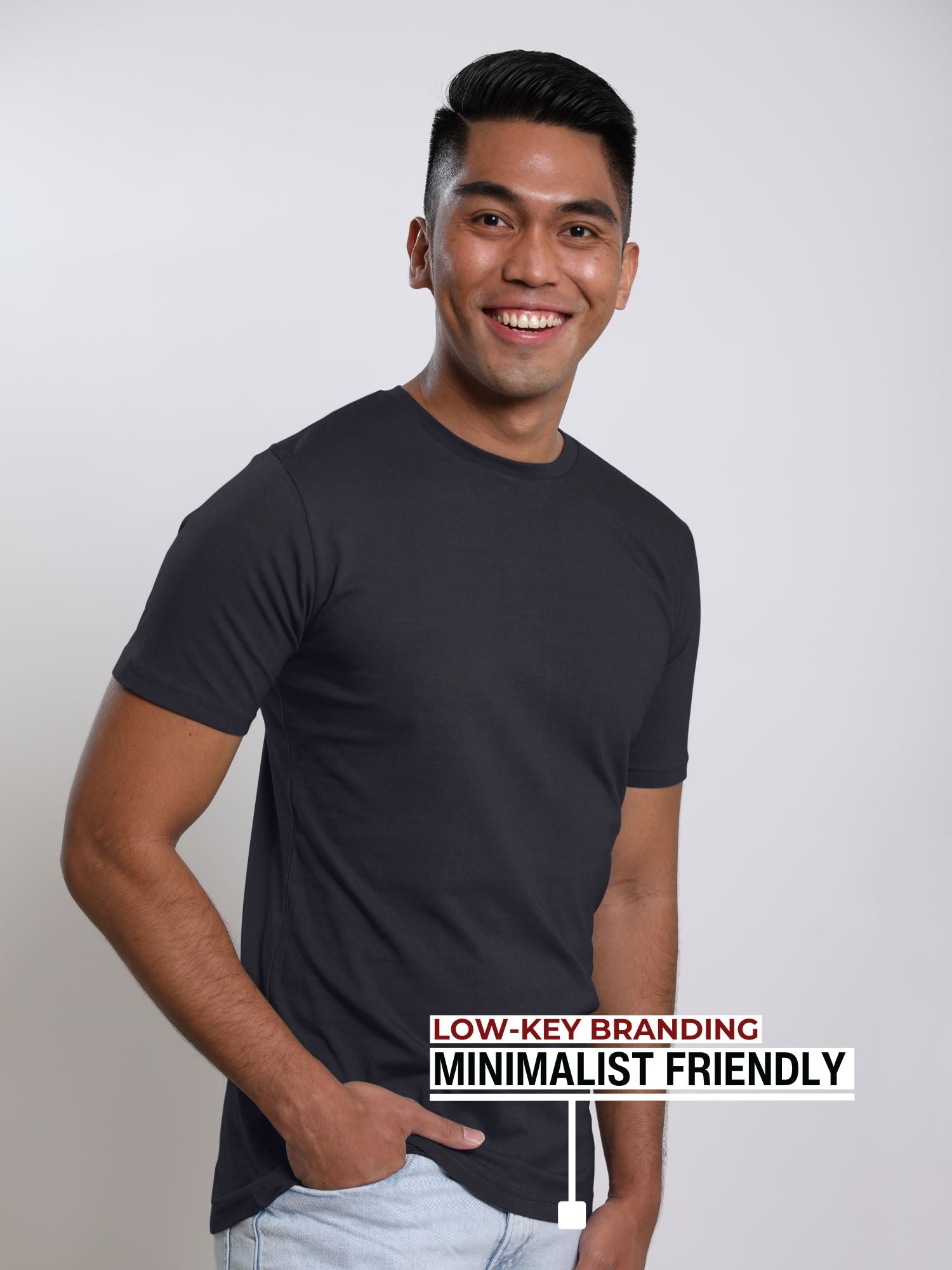 An upper body shot of a tall slim guy in a studio and wearing a charcoal medium tall t-shirt, hand in pocket.