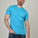 A tall and slim man in the studio standing in front of a light background. The smiling model is wearing an extra long slim cyan t-shirt in a size XL. The tall cyan t-shirt features a 3" longer body, 100% organic cotton, and is soft & preshrunk. The cyan t-shirt is ideal for tall slim men 6'2"+.