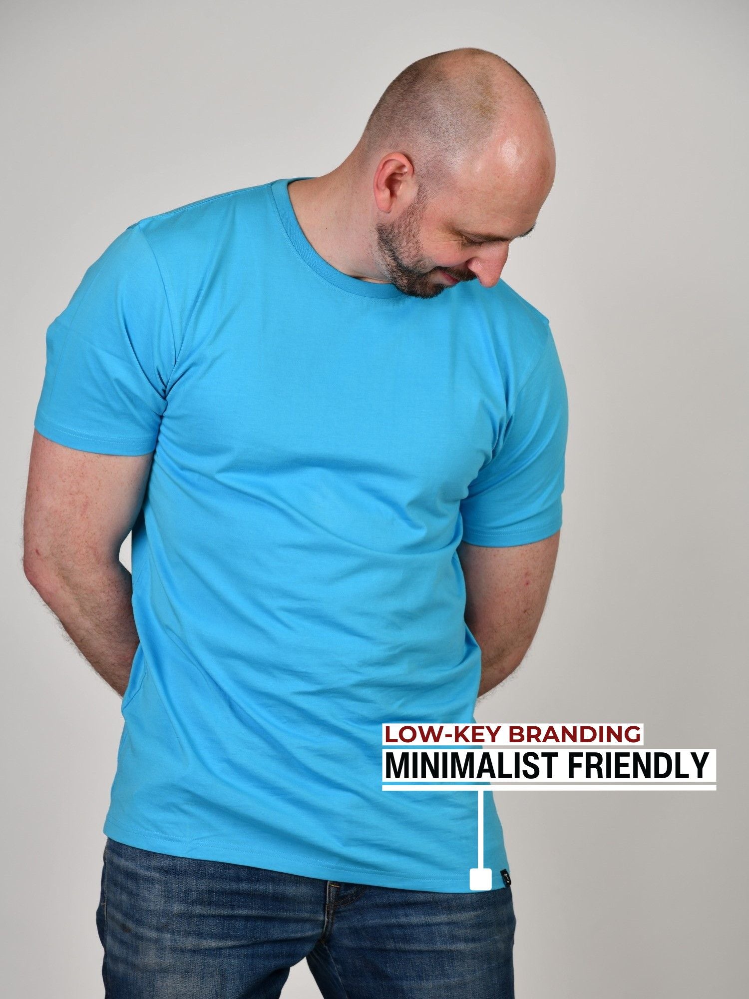 An upper body shot of a tall athletic guy in a studio and wearing a cyan extra large tall slim t-shirt and looking down at the monogram logo.