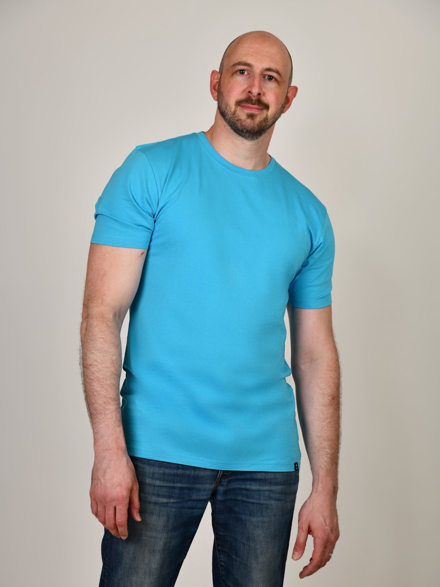 An upper body shot of a tall athletic guy in a studio and wearing a cyan extra large tall slim t-shirt.