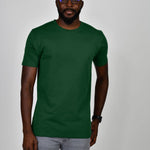 A tall and slim man in the studio standing in front of a light background. The smiling model is wearing an extra long slim dark green t-shirt in a size large. The tall dark green t-shirt features a 3" longer body, 100% organic cotton, and is soft & preshrunk. The  dark green t-shirt is ideal for tall slim men 6'2"+.