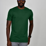 A tall and slim man in the studio standing in front of a light background. The smiling model is wearing an extra long slim dark green t-shirt in a size large. The tall dark green t-shirt features a 3" longer body, 100% organic cotton, and is soft & preshrunk. The dark green t-shirt is ideal for tall slim men 6'2"+.