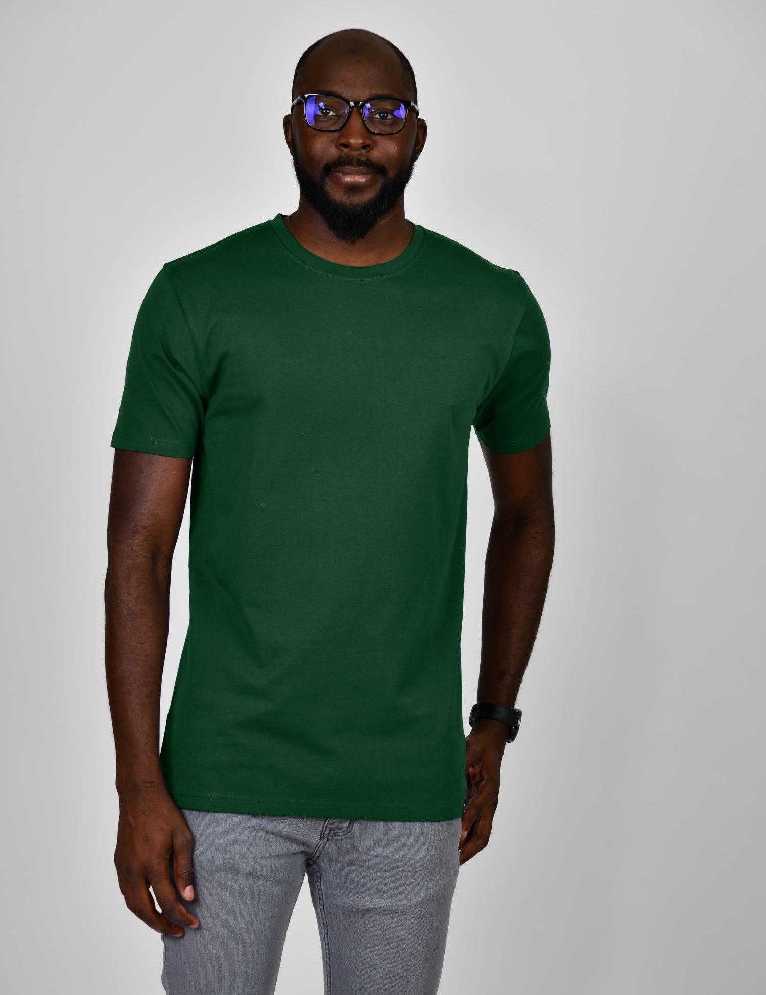 A tall and slim man in the studio standing in front of a light background. The smiling model is wearing an extra long slim dark green t-shirt in a size large. The tall dark green t-shirt features a 3" longer body, 100% organic cotton, and is soft & preshrunk. The  dark green t-shirt is ideal for tall slim men 6'2"+.