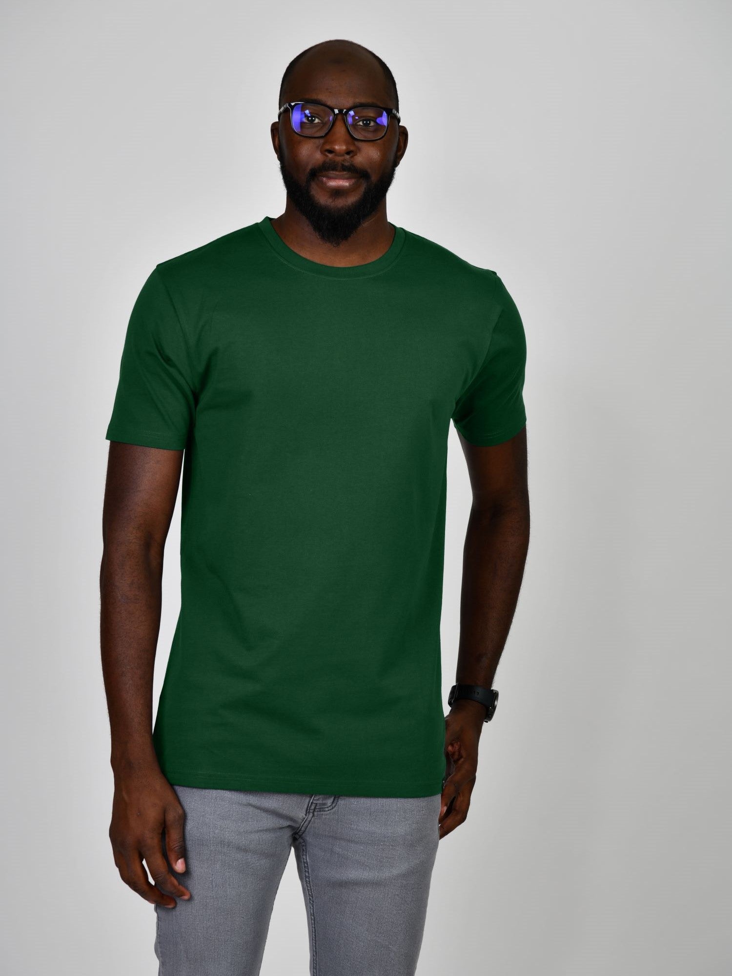 A tall and slim man in the studio standing in front of a light background. The smiling model is wearing an extra long slim dark green t-shirt in a size large. The tall dark green t-shirt features a 3" longer body, 100% organic cotton, and is soft & preshrunk. The dark green t-shirt is ideal for tall slim men 6'2"+.