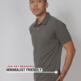 An upper body shot of a tall slim guy in a studio and wearing a medium tall slim dark grey polo shirt and showing the minimal Just Tall flag logo near the bottom of the side seam.