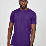 A tall and slim man in the studio standing in front of a light background. The smiling model is wearing an extra long slim royal purple t-shirt in a size large. The tall royal purple t-shirt features a 3" longer body, 100% organic cotton, and is soft & preshrunk. The royal purple t-shirt is ideal for tall slim men 6'2"+.