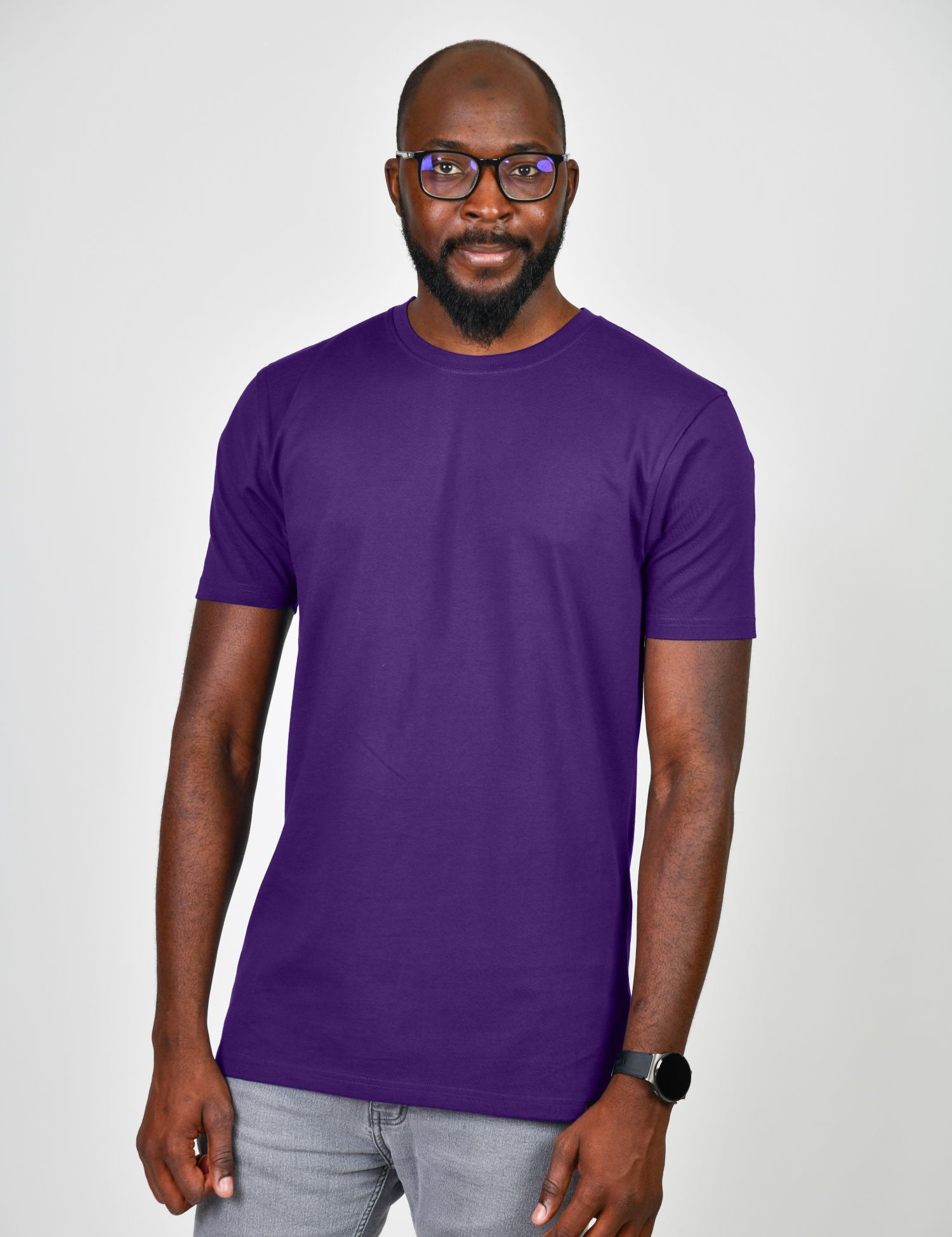 A tall and slim man in the studio standing in front of a light background. The smiling model is wearing an extra long slim royal purple t-shirt in a size large. The tall royal purple t-shirt features a 3" longer body, 100% organic cotton, and is soft & preshrunk. The  royal purple t-shirt is ideal for tall slim men 6'2"+.