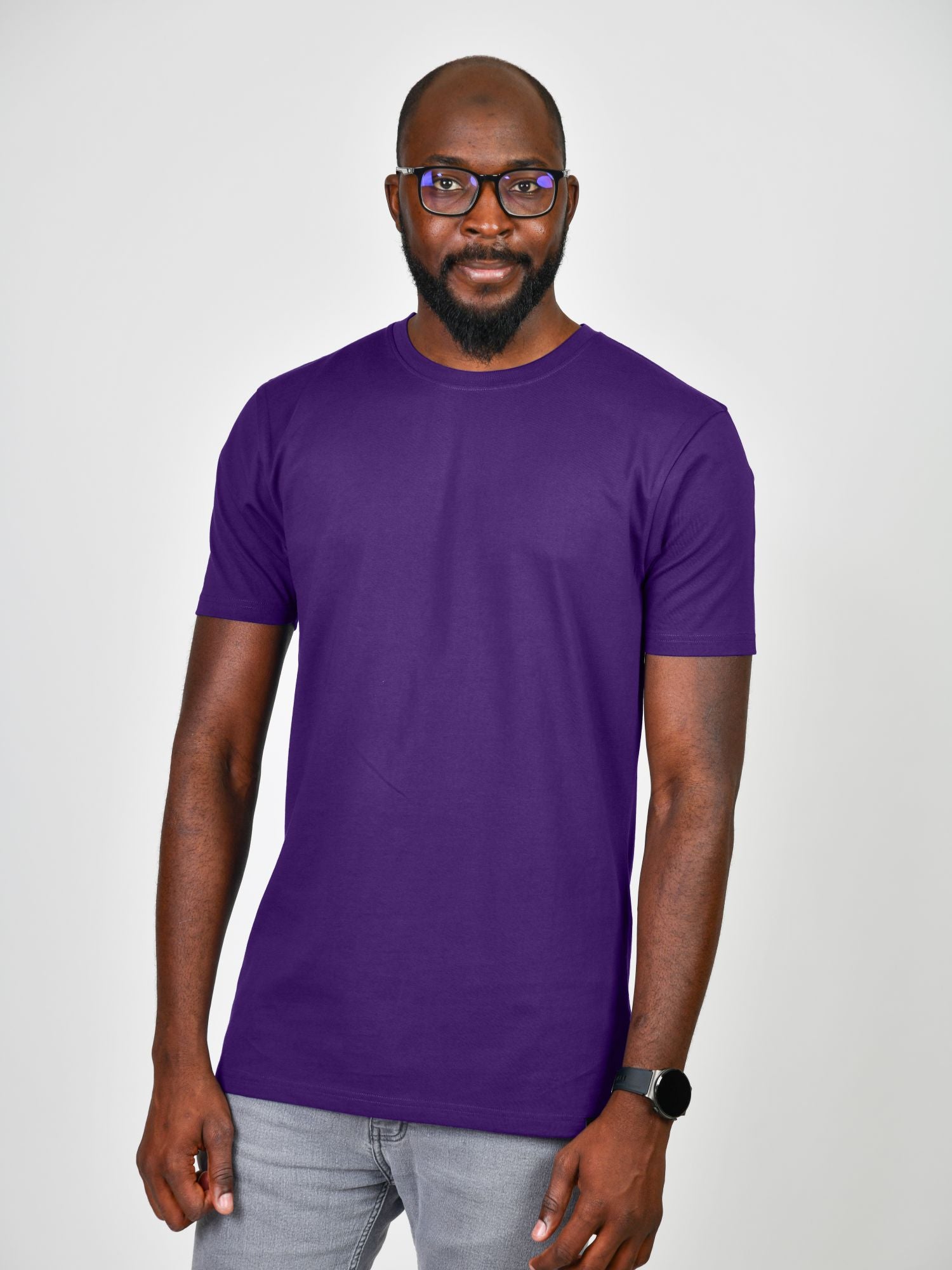 A tall and slim man in the studio standing in front of a light background. The smiling model is wearing an extra long slim royal purple t-shirt in a size large. The tall royal purple t-shirt features a 3" longer body, 100% organic cotton, and is soft & preshrunk. The royal purple t-shirt is ideal for tall slim men 6'2"+.