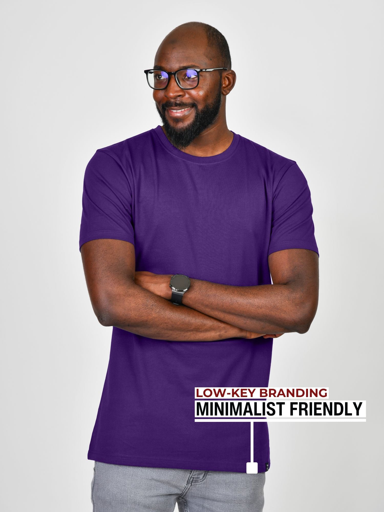 A tall slim guy standing in a studio and wearing a royal purple large tall t-shirt, smiling and arms folded.