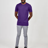 A head to toe shot of a tall slim guy in a studio and wearing a royal purple large tall slim t-shirt, hands behind back.