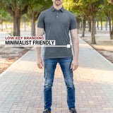 A head to toe shot of a tall athletic guy in a park and wearing an XL tall slim dark slate polo shirt and showing the minimal Just Tall flag logo near the bottom of the side seam.
