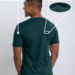 A shot from behind of a tall and slim guy in a studio and wearing a dark teal medium tall slim t-shirt.