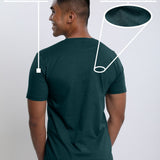 A shot from behind of a tall and slim guy in a studio and wearing a dark teal medium tall slim t-shirt.