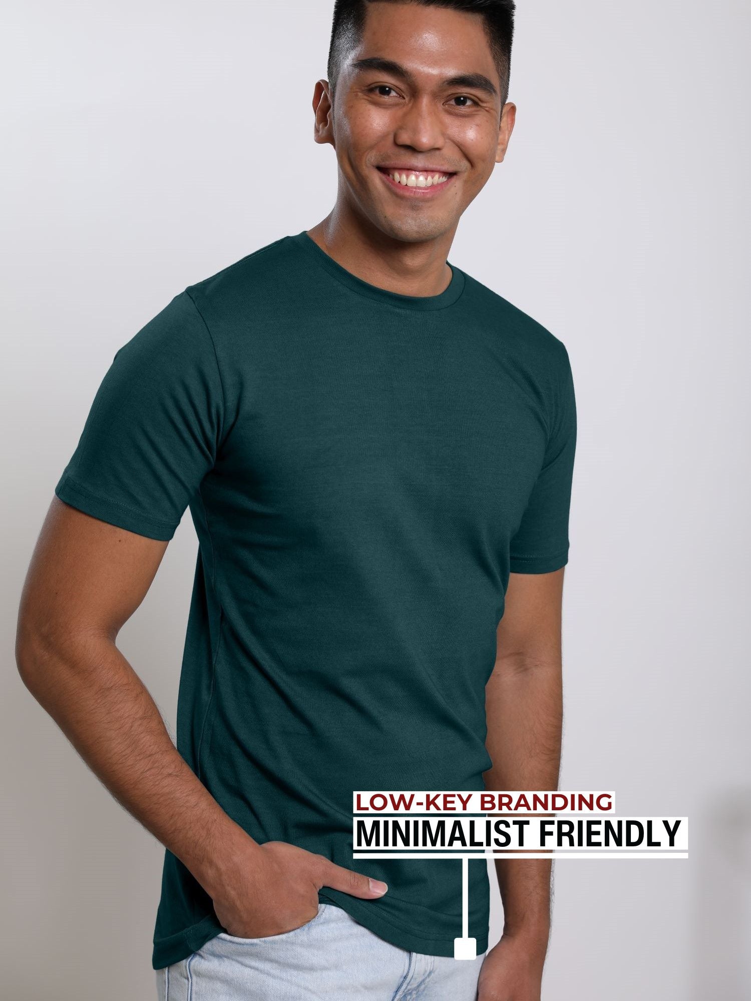An upper body shot of a tall slim guy in a studio and wearing a dark teal medium tall t-shirt, hand in pocket.