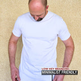 A tall slim man wearing an XL tall heavyweight white t-shirt and looking down at the Just Tall hem logo.