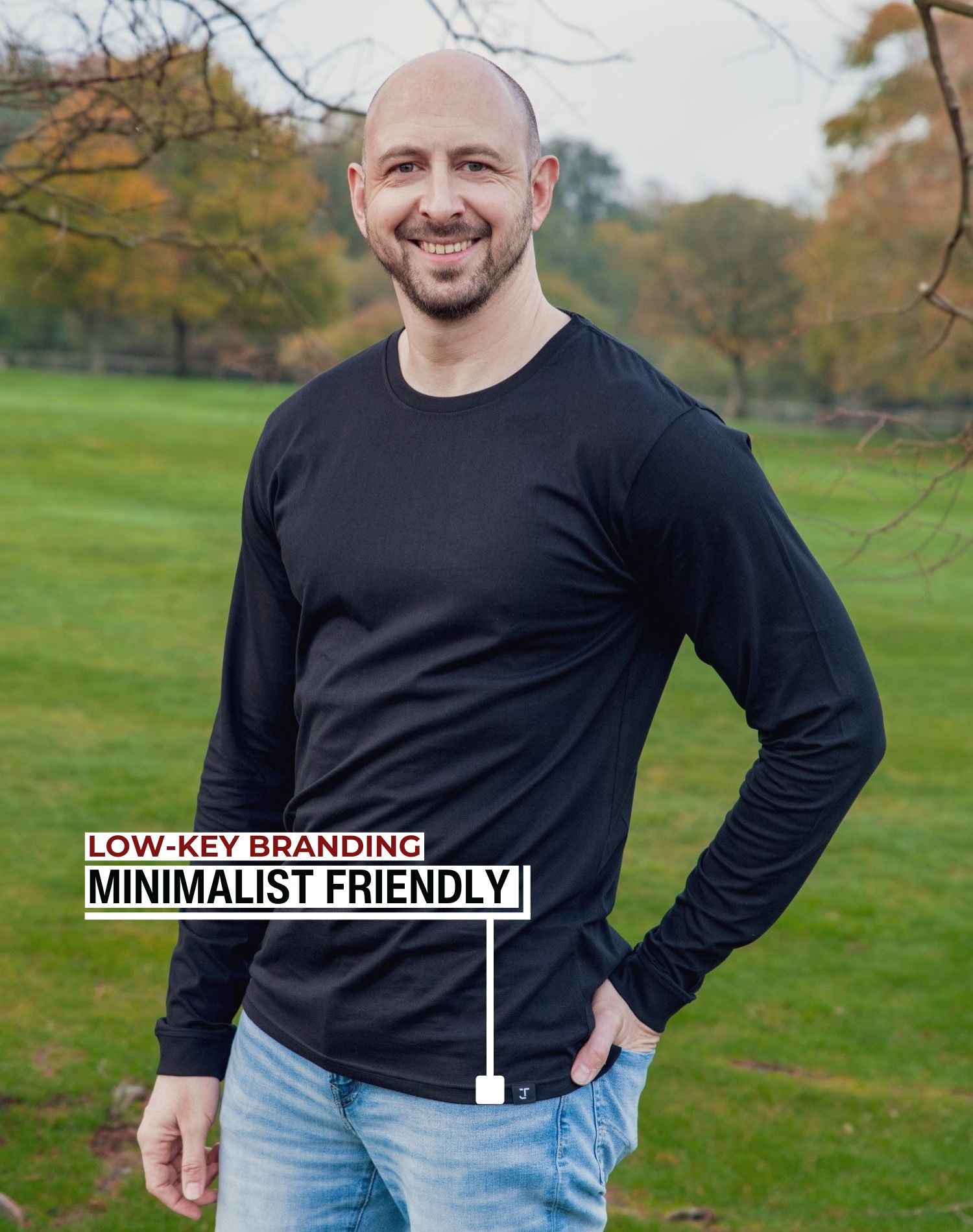 An upper body shot of a tall athletic guy standing in a park wearing a black extra long tall long sleeve t-shirt and showing the Just Tall minimalist monogram logo.