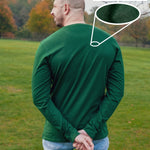 A shot from behind of a tall slim guy in a park wearing an extra long sleeve long sleeve tall t-shirt in green.