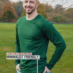 An upper body shot of a tall athletic guy standing in a park wearing a dark green extra long tall long sleeve t-shirt and showing  the Just Tall minimalist monogram logo.