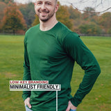 An upper body shot of a tall athletic guy standing in a park wearing a dark green extra long tall long sleeve t-shirt and showing the Just Tall minimalist monogram logo.