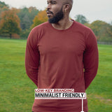 An upper body shot of a tall athletic guy standing in a park wearing a dark orange extra long tall long sleeve t-shirt and showig the the Just Tall minimalist monogram logo.