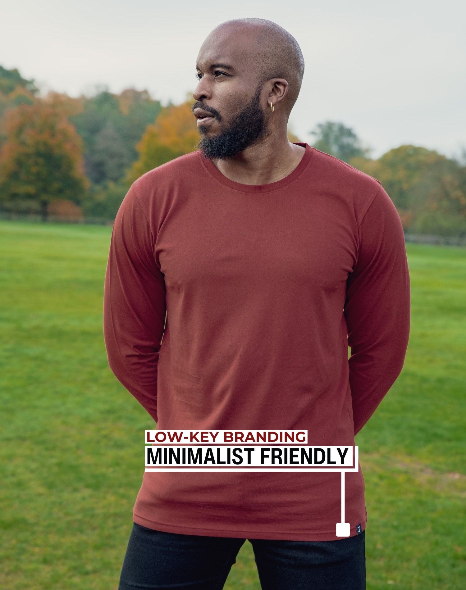 An upper body shot of a tall athletic guy standing in a park wearing a dark orange extra long tall long sleeve t-shirt and showig the the Just Tall minimalist monogram logo.