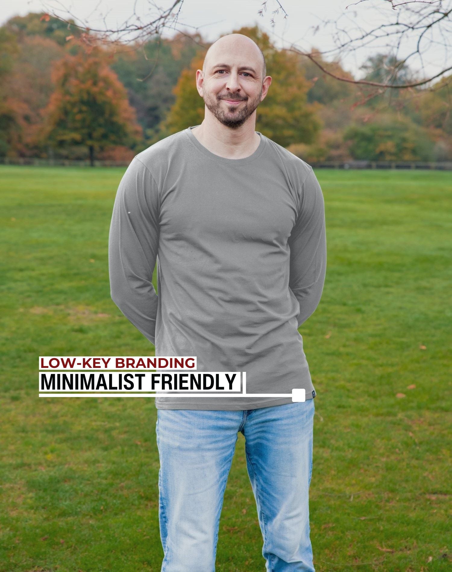An upper body shot of a tall athletic guy standing in a park wearing a light grey extra long tall long sleeve t-shirt and showing the Just Tall minimalist monogram logo.