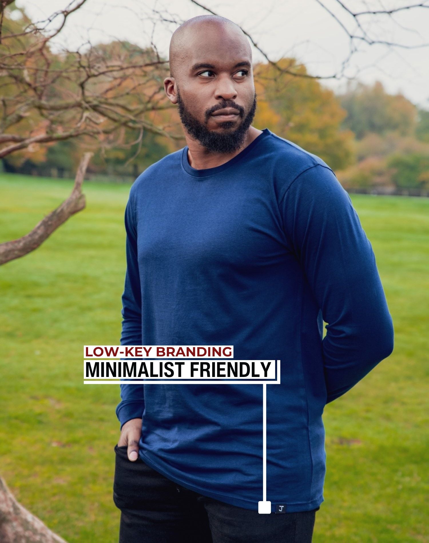 An upper body shot of a tall athletic guy standing in a park wearing a navy extra long tall long sleeve t-shirt and showing the Just Tall minimalist monogram logo.