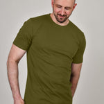 A tall and slim man in the studio standing in front of a light background. The smiling model is wearing an extra long slim olive t-shirt in a size XL. The tall olive t-shirt features a 3" longer body, 100% organic cotton, and is soft & preshrunk. The olive t-shirt is ideal for tall slim men 6'2"+.