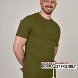 A tall athletic guy standing in a studio and wearing ab olive XL tall t-shirt, smiling and hands behind back.