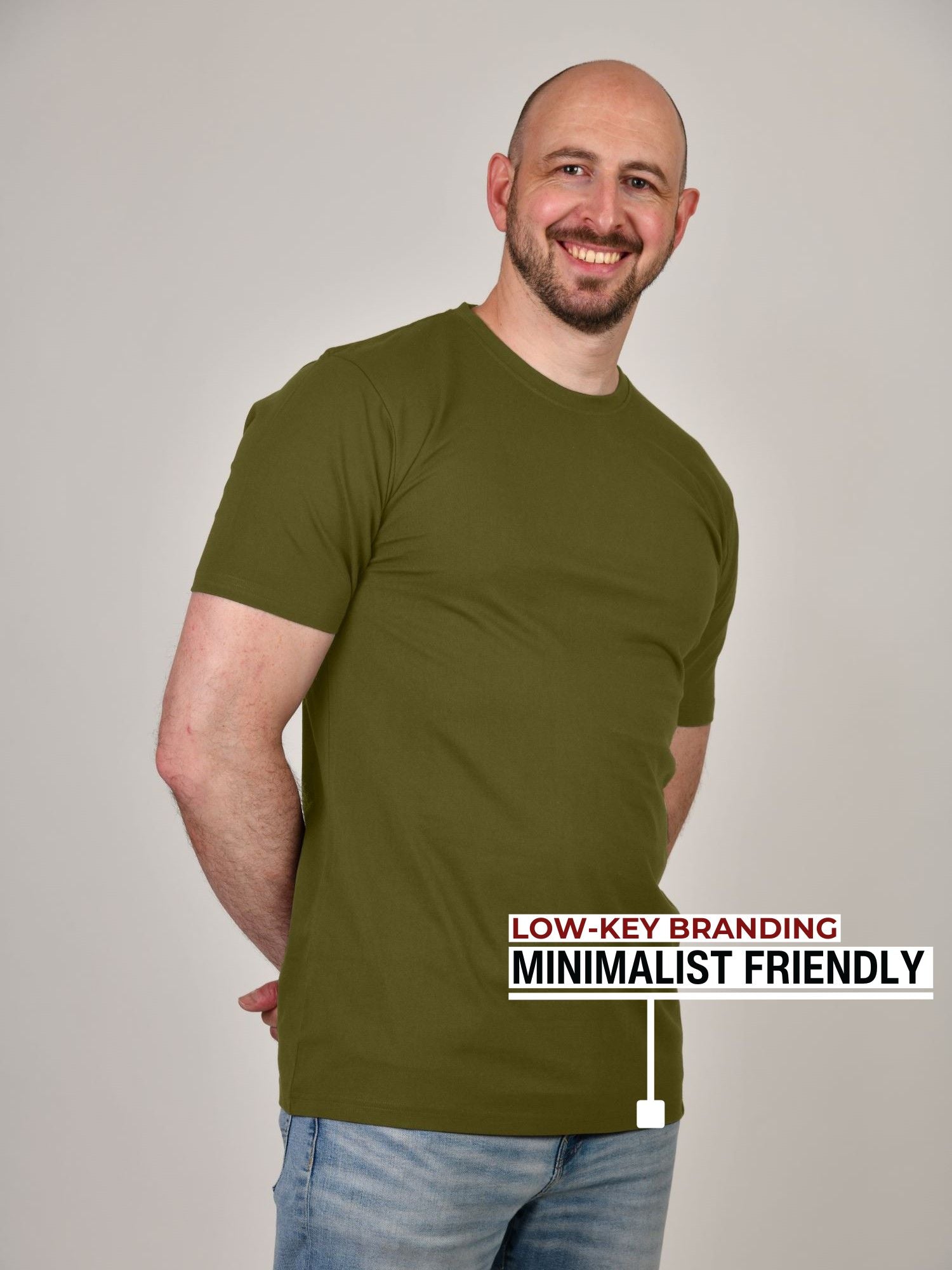 A tall athletic guy standing in a studio and wearing ab olive XL tall t-shirt, smiling and hands behind back.